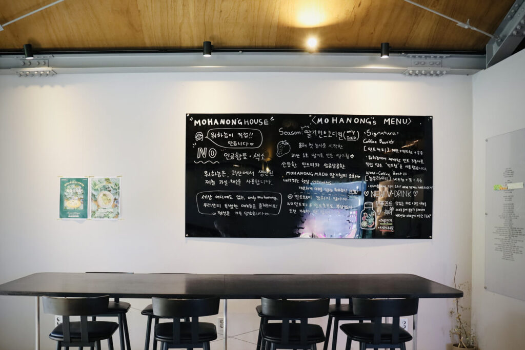 애견 동반 카페 뭐하농 하우스(Mohanong house)의 한쪽 흰색 벽에 붙어 있는 메뉴에 대한 설명이 쓰인 검정색 보드판