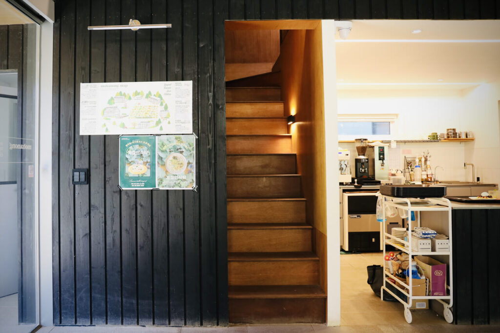 뭐하농 하우스 (Mohanong house) 의 실내에 있는 세로 결의 검은색 목재 벽면 옆에 있는 갈색의 목재 계단