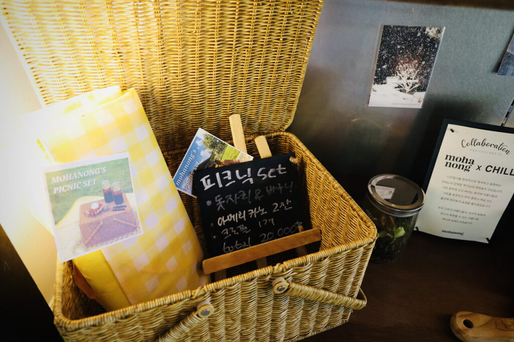 노란색 돗자리와 피크닉 세트를 소개하는 검은색 보드판이 담겨있는 노란색 바구니