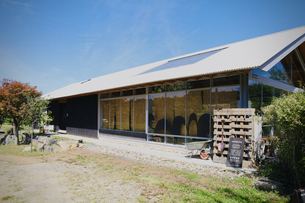 검은색 목재와 통유리로 이루어진 벽면, 그리고 경사 지붕으로 이루어진 뭐하농 하우스(Mohanong house)의 카페 건물