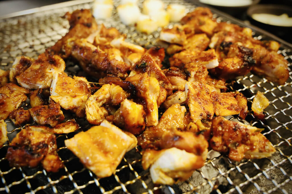 숯불 위 철판에 잘게 잘라 놓인 샘토 명물 닭갈비의 붉은색 양념 닭갈비